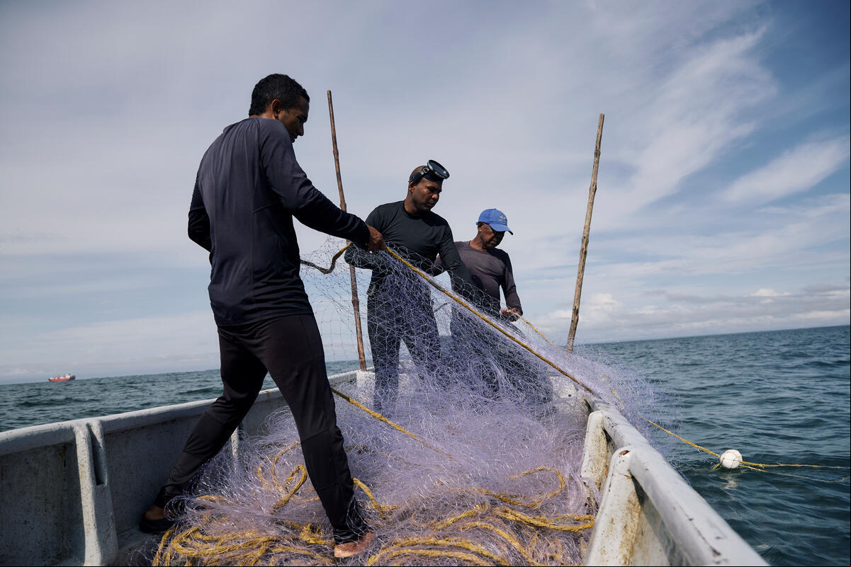 Tres hombres afro recogen una red de pesca sobre una embarcación